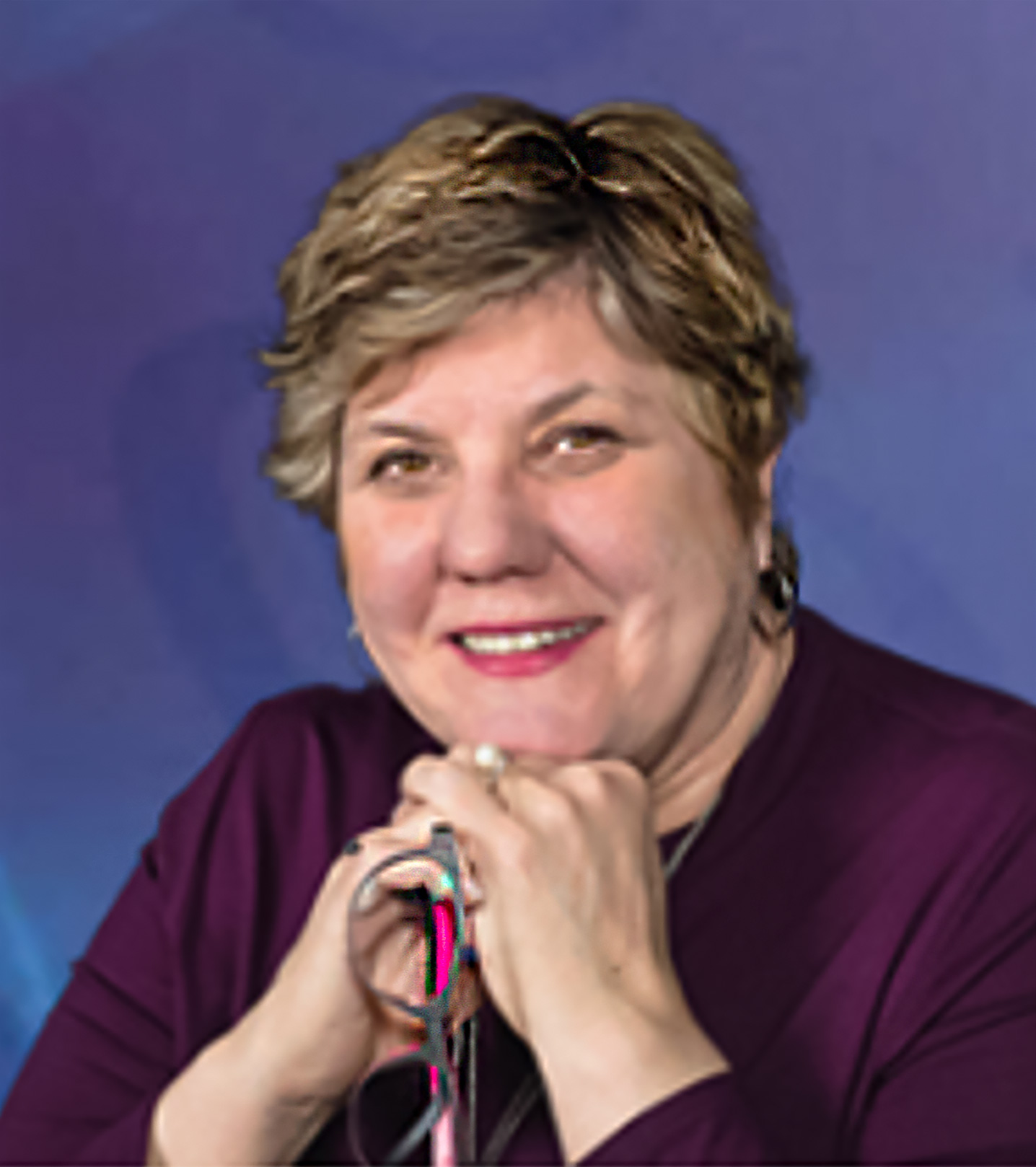 Close-up portrait photograph of Patricia Flatley Brennan, RN, Ph D. smiling with clasped hands under her chin.