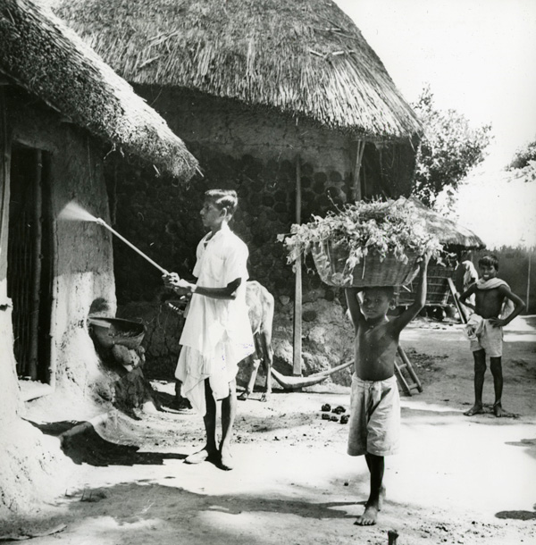 A man holds a spraying tool against an exterior wall, while two youths stand near.