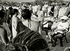 Black and white photograph of people, some wearing traditional Native Hawaiian garb, standing in a loose circle.