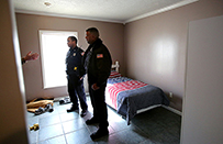 Two police officers looking at a person on the left whose hand sticks out from behind a wall.