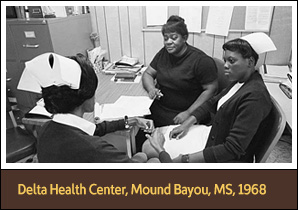 Three African American women sit around a desk; two are wearing nursing caps.