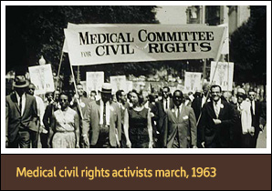 Large multiracial group of men and women holding signs and marching on a street towards viewer