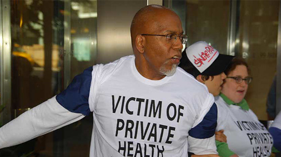 Three protesters linking arms in lobby, wearing shirts that say 'Victim of private health insurance.'