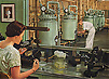 A woman seated at a laboratory bench examines a petri dish under a magnifying glass.  In the background a man examines an industrial fermentation tank.