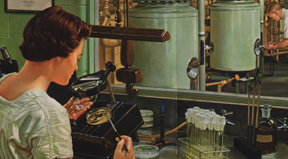 A woman seated at a laboratory bench examines a petri dish under a magnifying glass.  In the background a man examines an industrial fermentation tank.