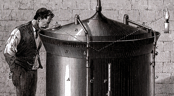 A man stands next to a large cylindrical beer vat and gazes into the vat through a small opening in the conical cover.