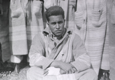 A Cherokee Indian patient sits cross legged and armed on the ground. He is wearing a robe with a cross on the left breast with a bandage on his injured left hand. World War I. U.S. Base Hospital No. 41, Paris, France, c.1917-18. Image A05587 from Images from the History of Medicine (IHM).