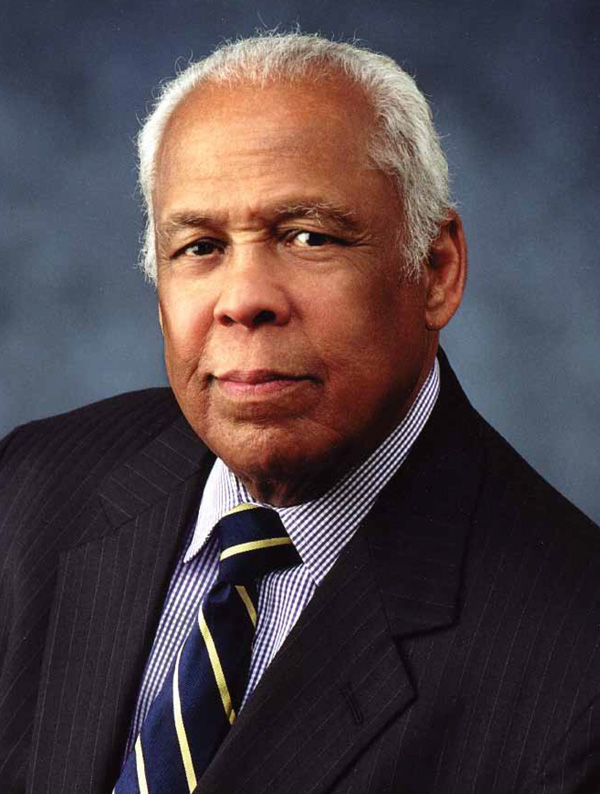 A man’s portrait wearing a black suit coat with a dress shirt and tie.