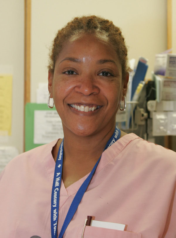 A woman smiling in pink medical scrubs.