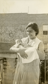 Smiling white woman holding newborn baby outside.