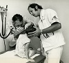 Two White men wearing white, examine the ear of a seated White girl.