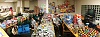 Large group of people stand amidst tables filled with food items.