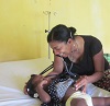 A woman smiling and wearing a stethoscope looks down at a girl on an examination table.