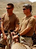 Two White men in military camouflage stand holding the reins of a donkey. 