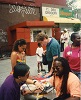 Asian American man checks the blood pressure of an African American man on a street.