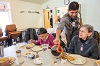 Hispanic man pours coffee between two seated elderly women.