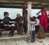 A seated White woman tends to an elderly South Asian woman with others looking on.