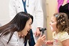 Asian woman smiles while looking into a White girl's mouth.