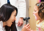 Asian woman smiles while looking into a White girl's mouth.