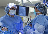 Three people in scrubs perform surgery, one looks off to the right at a screen out of view.