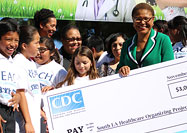 African American woman holds a large check, surrounded by a multiracial group of people.