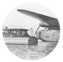 A man in uniform stands at the back of an quarantine inspection boat that is on the water near a sea plane in the Baltimore harbor.