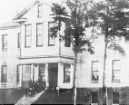 The front of the first marine hospital owned by the Federal Government. c. 1860. A group of people stand on the top of the steps of the hospital.