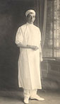 A White male nurse in white, stands in a studio and looks at the viewer.