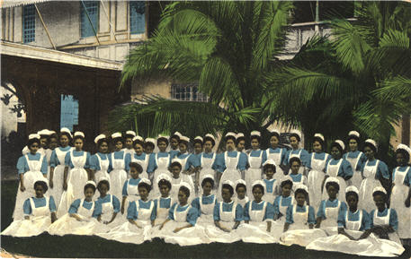 A large group of female nurses in blue and white sit for a group photograph in front of a building.