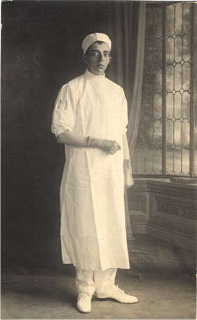 A White male nurse in white, stands in a studio and looks at the viewer.