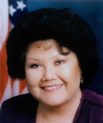 Dr. Kathleen R. Annette, an American Indian female smiling in front of the American flag.