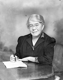 Dr. Emily Dunning Barringer, a White female in a collared blouse writing a letter at a desk.