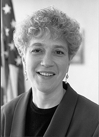 Dr. Lynn R Goldman, a White female with curly posing in front of an American flag.