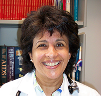 Du. Amneris E. Luque, a female in a lab coat and badge in front of a bookshelf.