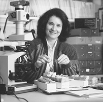 a White female looking at a tray of slides seated in a room with lab equipment.