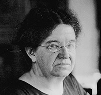 Dr. Florence Rena Sabin, a White female seated looking through a microscope.