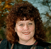 Dr. Susan Potts Sloan, a White female with curly hair posing outdoors for her portrait.