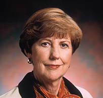 Dr. Virginia Verral Weldon, a White female in an orange ruffle blouse and suit jacket posing for her portrait.