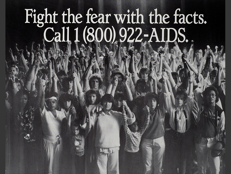 Black and white photograph with a multiracial group of adults and children holding each other’s hands above their heads.  