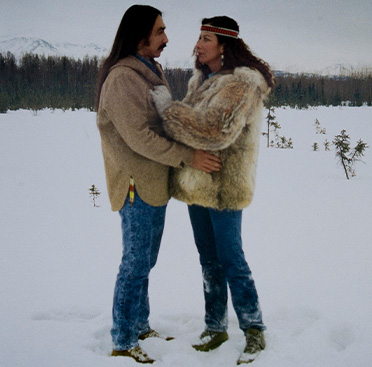 A poster with text and a color photograph of an Alaska Native man and woman embracing in a snow-covered field