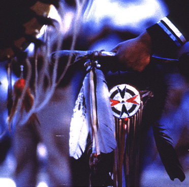 A poster with text and a color photograph of a hand holding a club with feathers attached.