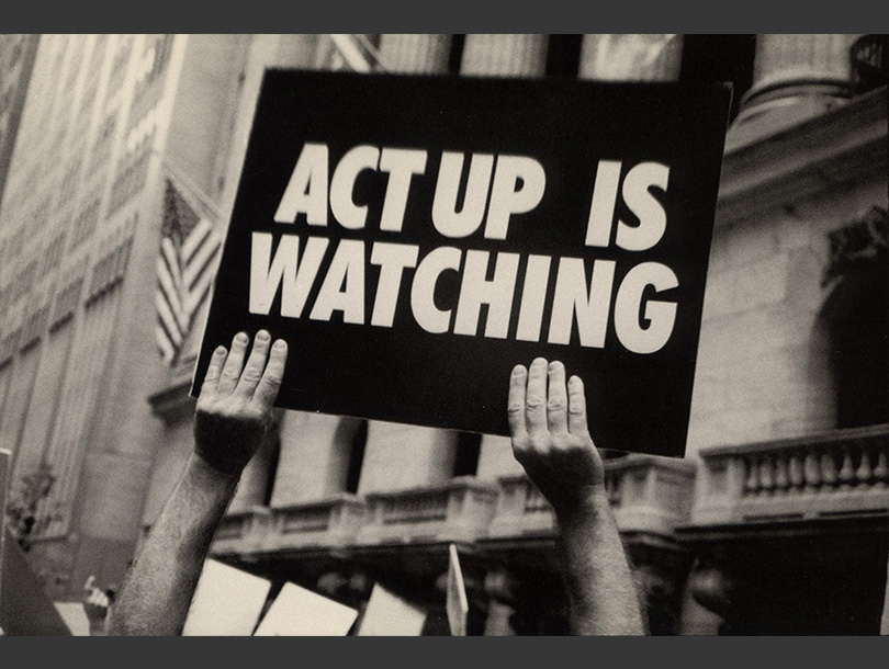 Black and white photograph of a pair of hands holding up a sign on a city street