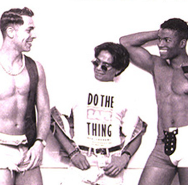 Black and white photograph of a multiracial group of men variously dressed waiting in line for a condom dispenser