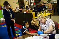 A white woman tests an African American girl for lead poisoning while another white woman looks on